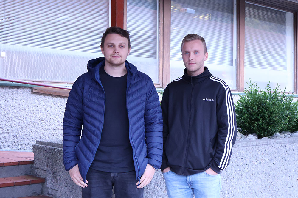 To unge vaksne menn står oppstilt saman og smilar lurt til kamera.