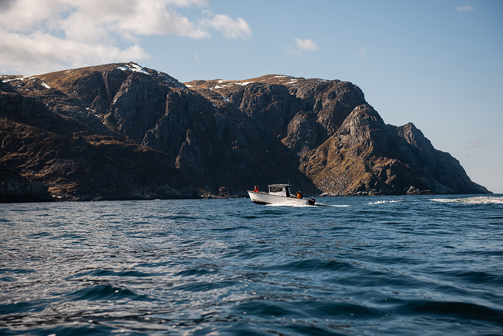 Liten båt hoppar på bølgjene. I bakgrunnen er eit mørkt fjell. Foto.