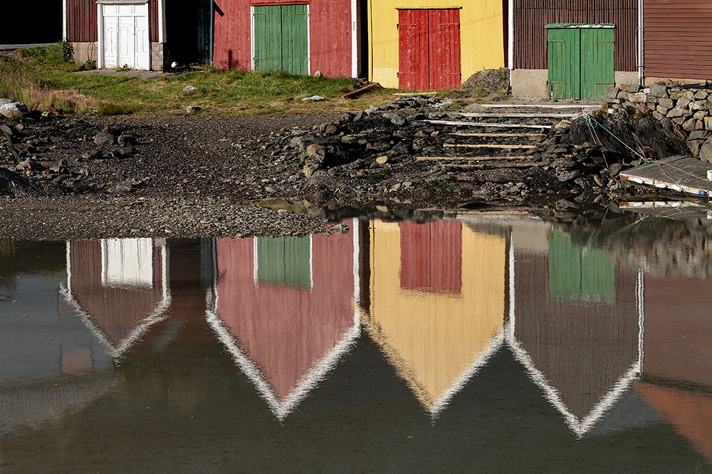 Tradisjonelle og fargerike naust er reflektert i vatnet nedanfor dei. Foto.