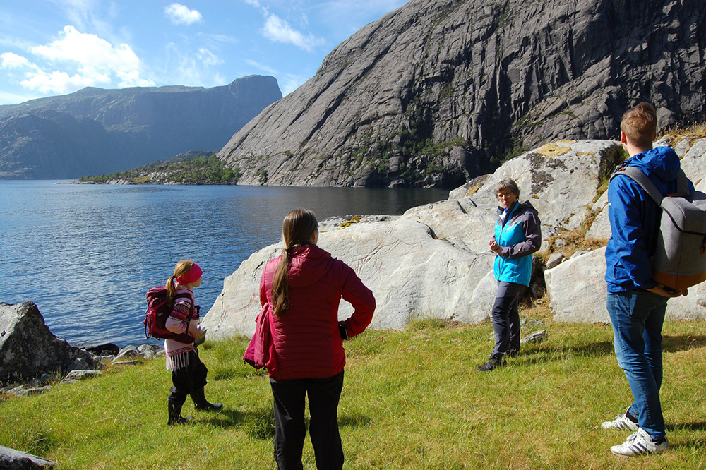 Guide forklarar historia til Vingen helleristningsfelt for tre personar. Foto.