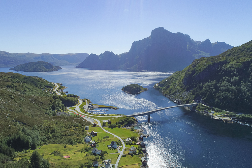 Oversiktsbilete av ein moderne bru som kryssar vatn. I bakgrunnen er det eit stort kantete fjell, Hornelen. Foto.