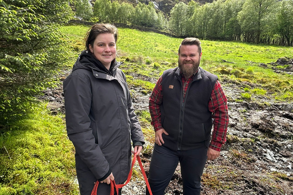 Kvinne og mann står oppstilt på ei mark og smiler til kamera. Foto.