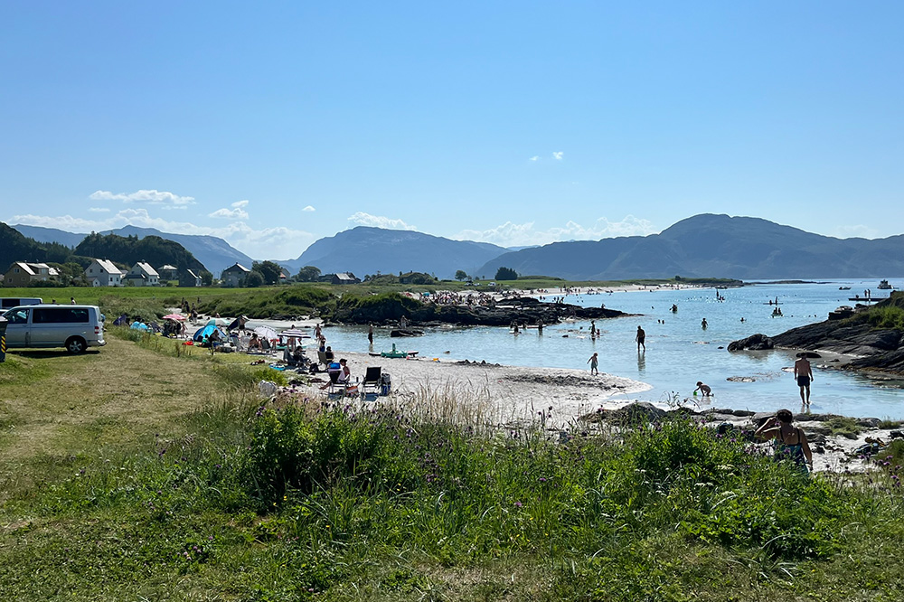 Folksam sandstrand, med mange på stranda og i sjøen. Foto.
